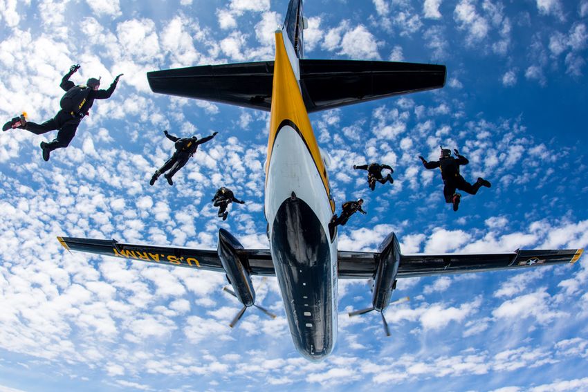 six men jumping out of a plane with parachutes on